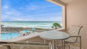 A balcony with a view of the ocean, a pool, and a table with chairs.