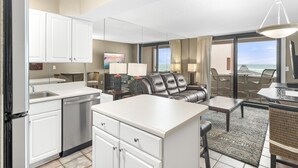 A modern hotel room with a kitchen, dining area, and a balcony with a view of the ocean.