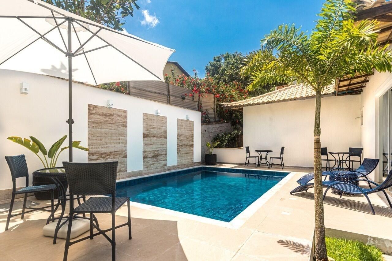 A swimming pool with lounge chairs and a table, surrounded by a tiled patio and a small garden area.