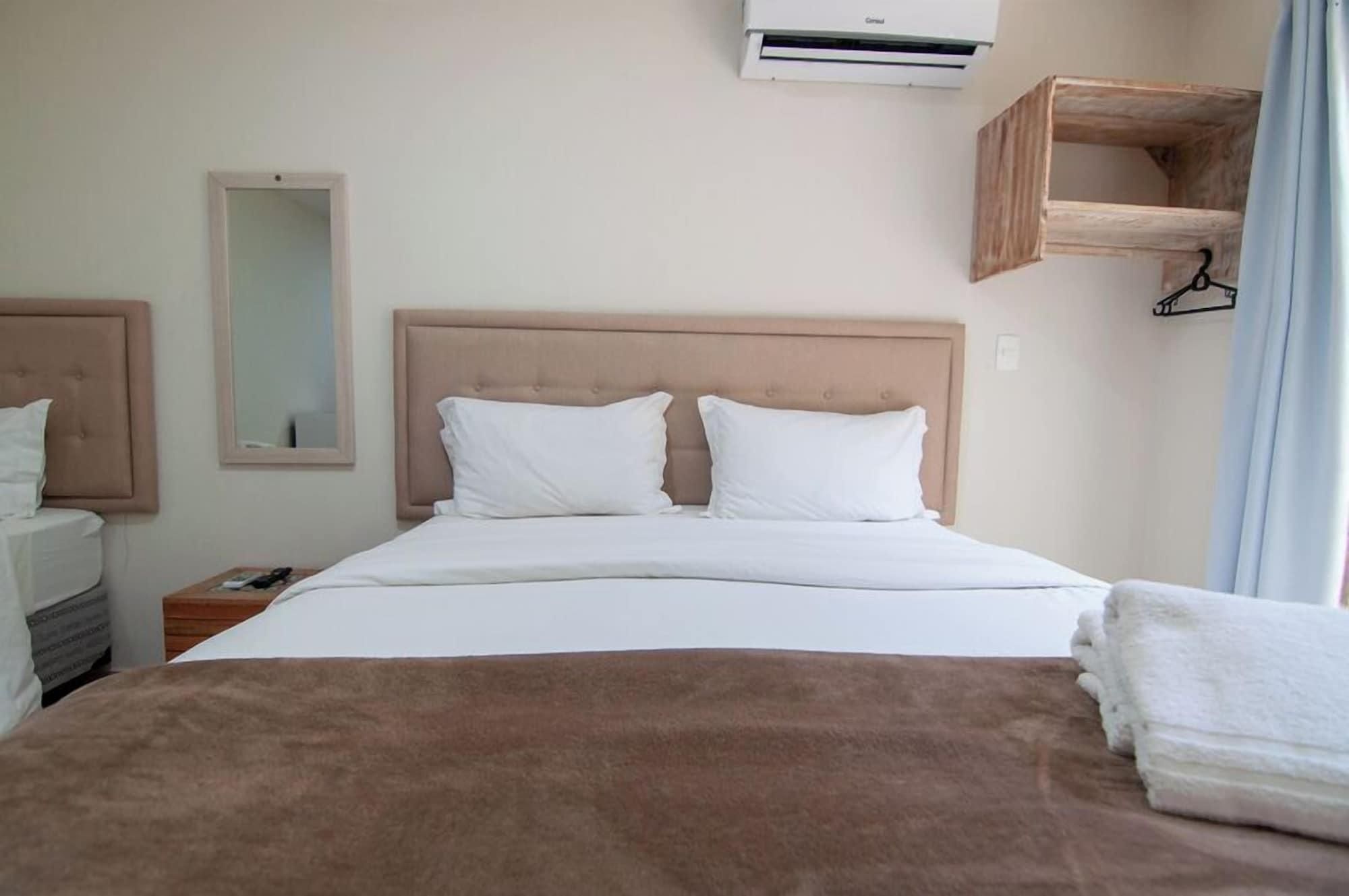 Een hotelkamer met een bed, nachtkastje, spiegel, airconditioning en een houten plank.