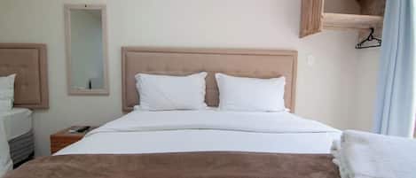 A hotel room with a bed, a bedside table, a mirror, an air conditioning unit, and a wooden shelf.