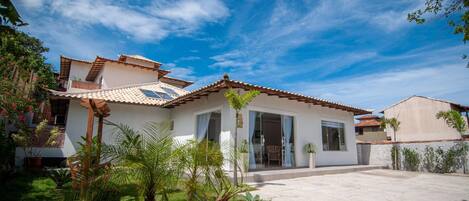 A two-story house with a tiled roof, a front porch, and a well-maintained garden with palm trees and shrubs.