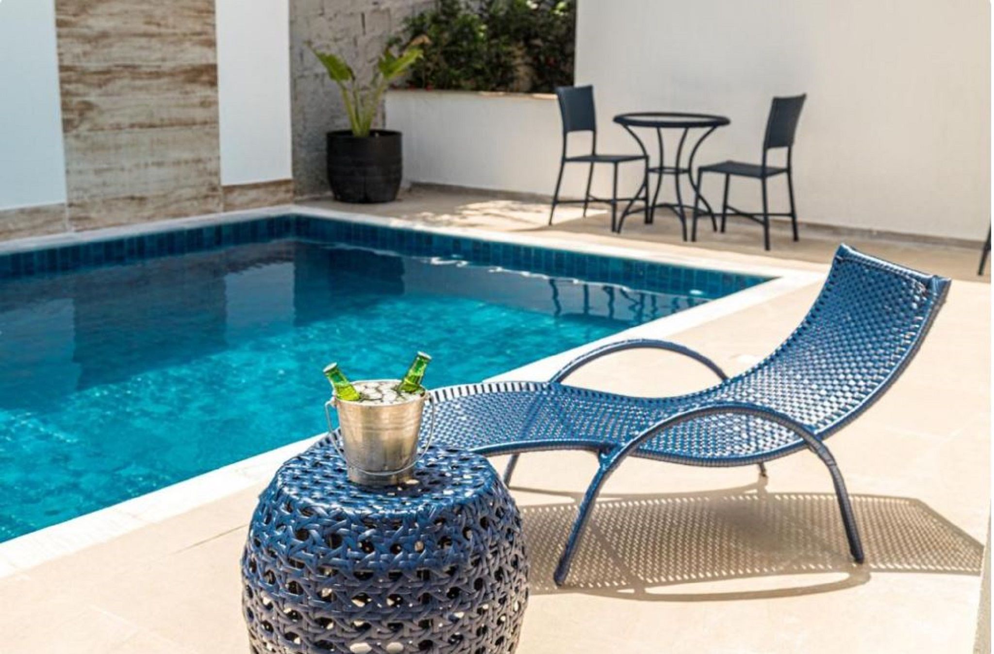 A poolside area with a blue metal chair, a round table with a metal bucket, and a potted plant.