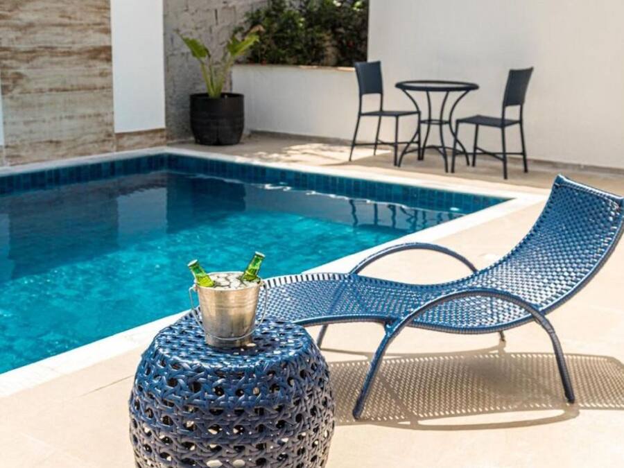Zona de piscina con una silla metálica azul, una mesa redonda y un cubo metálico, además de una planta en maceta.