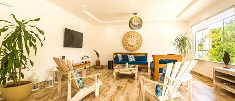 Ein geräumiges Wohnzimmer mit einem blauen Sofa, Holzstühlen, einem Couchtisch und einer großen Küstpflanze.