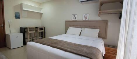 A bedroom with a bed, a desk, a chair, an air conditioner, and a wardrobe.