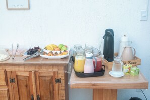 A breakfast setup with fruits, drinks, and coffee equipment on a wooden table.
