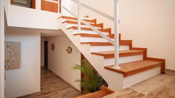 Una escalera moderna con peldaños de madera y barandillas blancas, que conduce a un piso superior con una puerta de madera y un ventanal.
