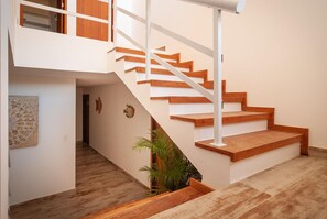 A modern staircase with wooden steps and white railings, leading to an upper floor with a wooden door and a window. - Pousada Maktub (Búzios)