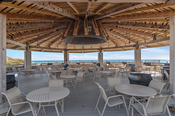 A covered outdoor seating area with tables and chairs, overlooking a beach. - Jetty view enclosed balcony. One free beach chair set up daily. (Destin)