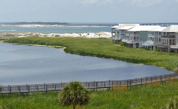 A waterfront property with a curved water body, a wooden boardwalk, and a row of buildings with balconies. - Gorgeous, enclosed balcony unit! One free beach set up daily. (Destin)