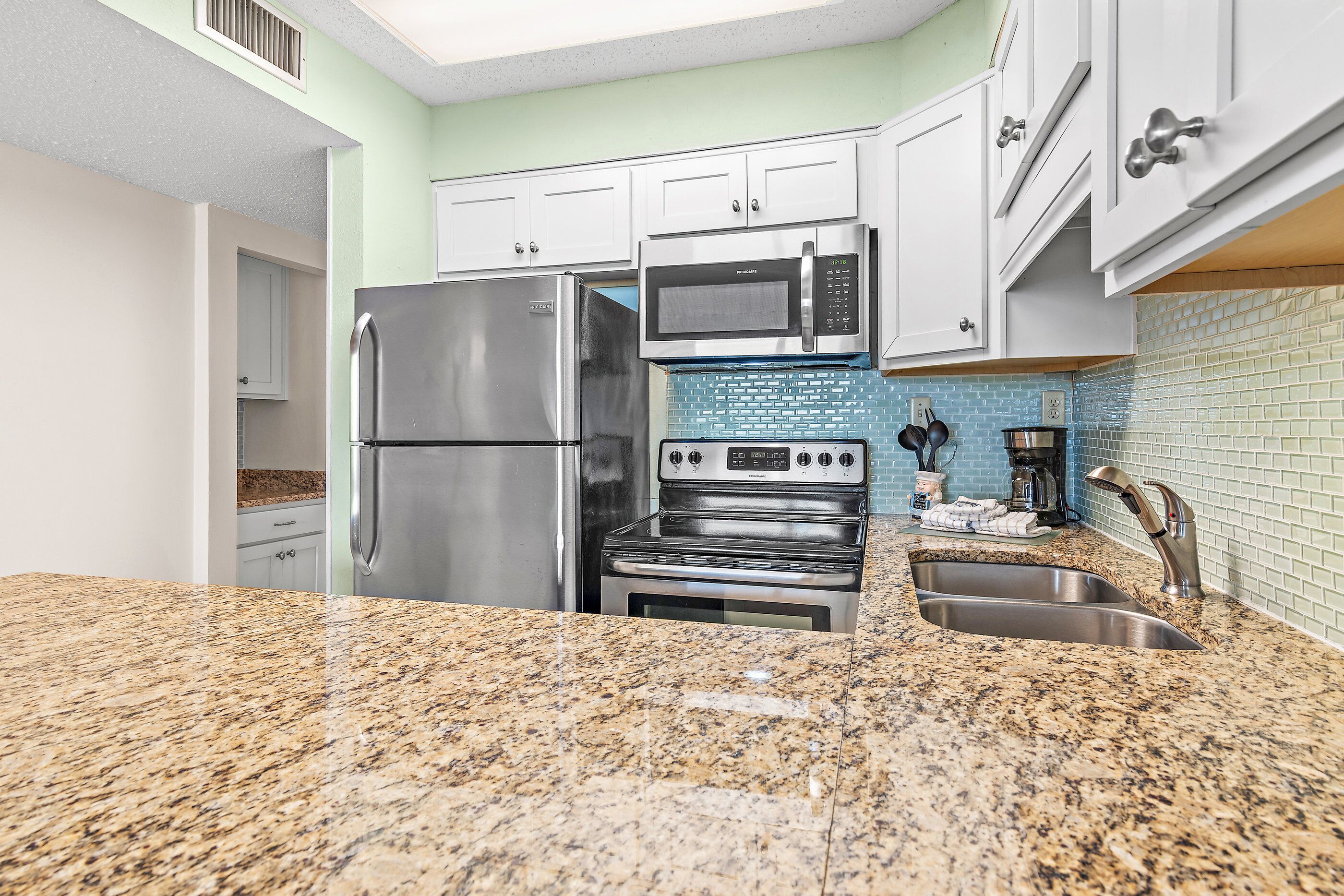 A kitchen with granite countertops, stainless steel appliances, white cabinets, and a blue-tiled backsplash.