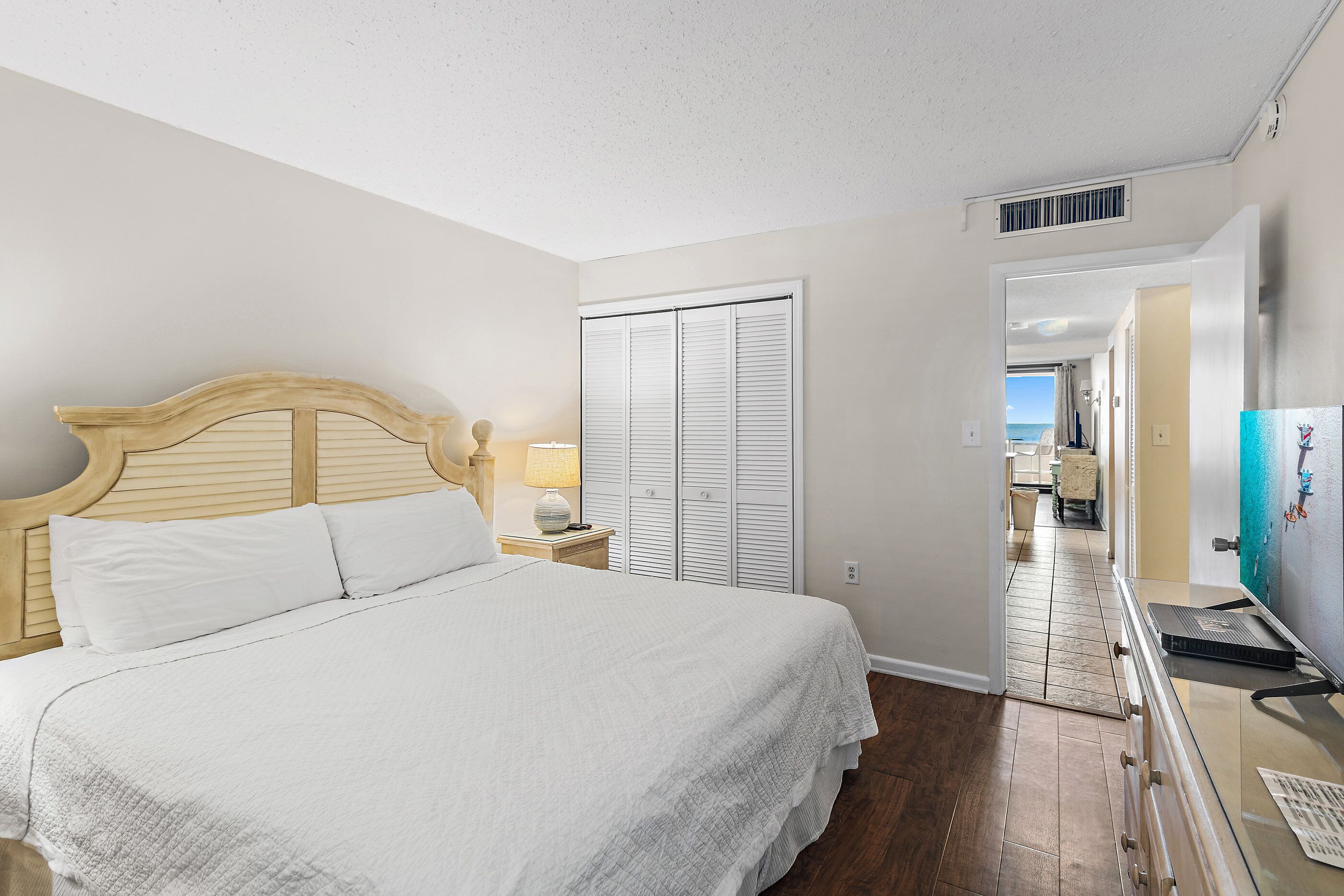 A bedroom with a bed, a nightstand, a lamp, a dresser, and a view of the outside.