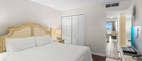 A bedroom with a bed, a nightstand, a lamp, a dresser, and a view of the outside.
