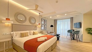 A modern hotel room with a large bed, a ceiling fan, a TV, a seating area with a sofa and chairs, and a large window with curtains. - Apartamentos Soho Boutique Palillero (Cádiz)