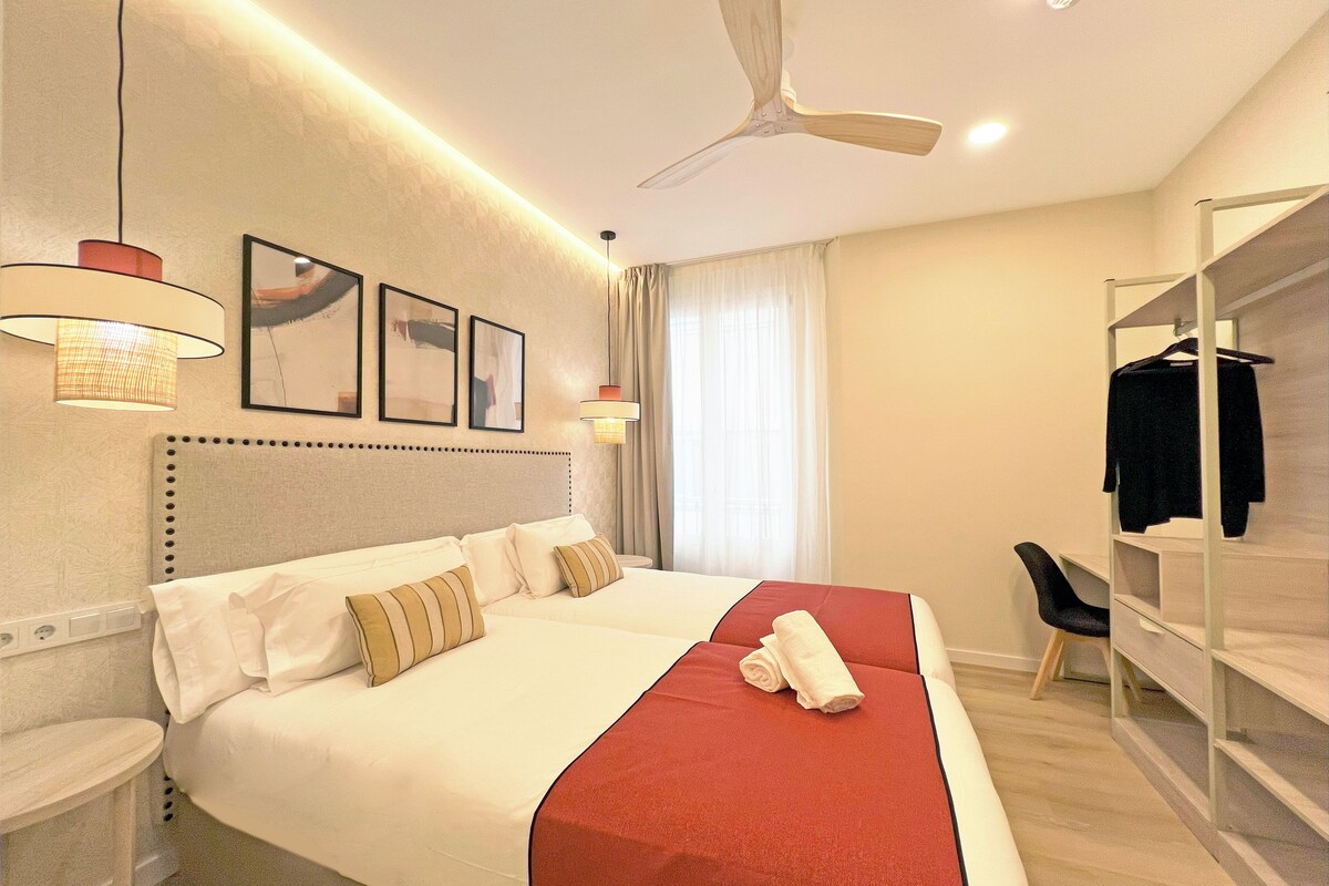 Une chambre d’hôtel avec un grand lit, un bureau, une chaise, une armoire et un ventilateur de plafond.