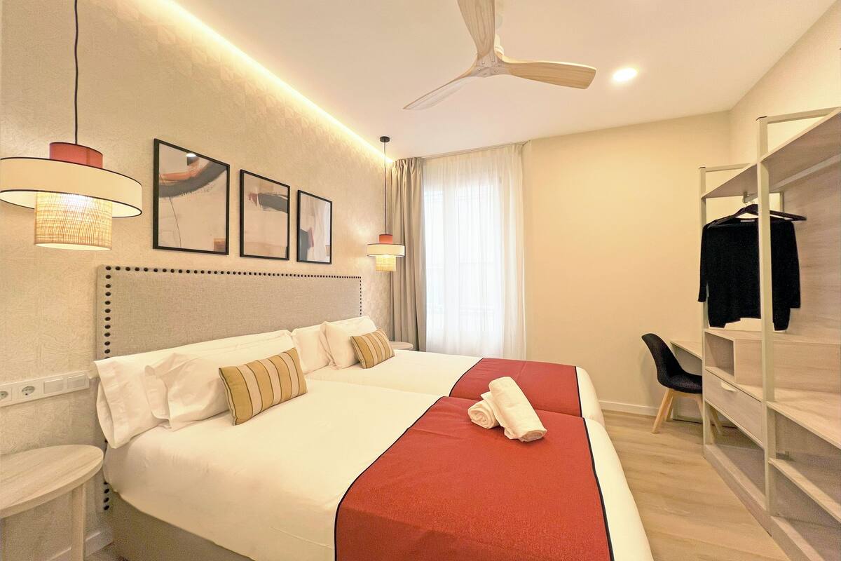 A hotel room with a large bed, a desk, a chair, a wardrobe, and a ceiling fan.