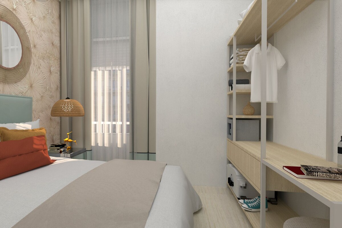 A modern hotel room with a large bed, a bedside table with a lamp, a wardrobe, and a mirror on the wall.