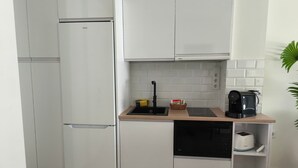 A compact kitchen with white cabinetry, a built-in dishwasher, a coffee maker, and a small sink. - Apartamentos Soho Boutique Palillero (Cádiz)
