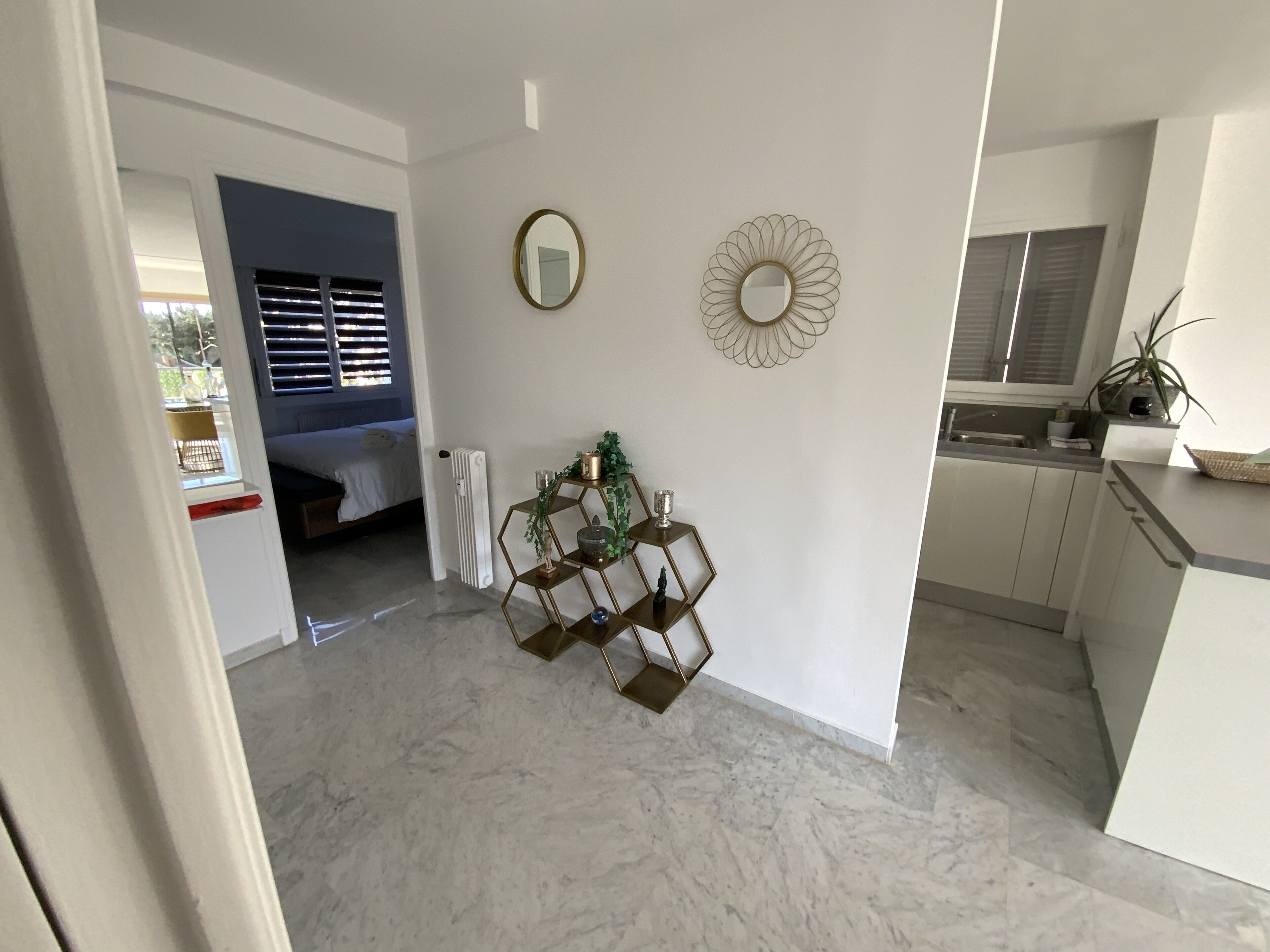 A modern kitchen with white cabinets, a marble floor, and a dining area with a hexagonal metal shelf.