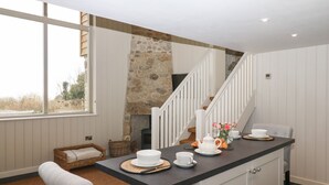 A modern kitchen with a stone wall, a dining area with a high ceiling, and a staircase. - Beckaford View (Newton Abbot)