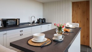 A modern kitchen with a dark countertop, a sink, a microwave, a coffee maker, and a wooden door. - Beckaford View (Newton Abbot)