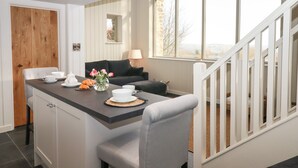 A modern kitchen with a dining area, featuring a wooden door, a black sofa, and a view of the outdoors through large windows. - Beckaford View (Newton Abbot)