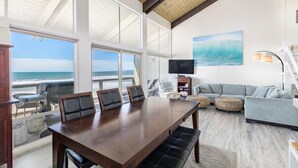 A spacious room with a large wooden dining table, comfortable seating, a television, and a view of the ocean. - Sand Dollar Beachfront Home, Direct Beach Access! (La Selva Beach)