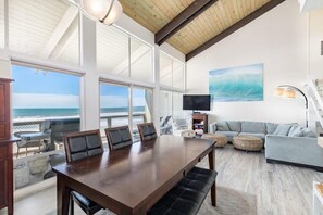A spacious room with a large wooden dining table, comfortable seating, a television, and a view of the ocean. - Sand Dollar Beachfront Home, Direct Beach Access! (La Selva Beach)