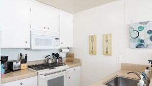 Une cuisine compacte équipée d’un four à micro-ondes, d’une cuisinière, d’un évier et de divers ustensiles.