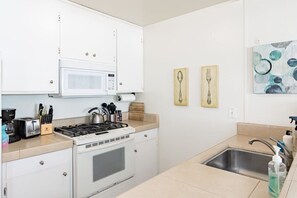 A compact kitchen with a microwave, stove, sink, and various utensils.