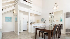 A spacious dining area with a long wooden table and chairs, a kitchen in the background, and a staircase leading to an upper level. - Sand Dollar Beachfront Home, Direct Beach Access! (La Selva Beach)