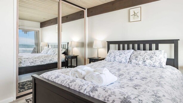 Une chambre avec un grand lit, une table de chevet, un miroir et une vue sur l’océan.