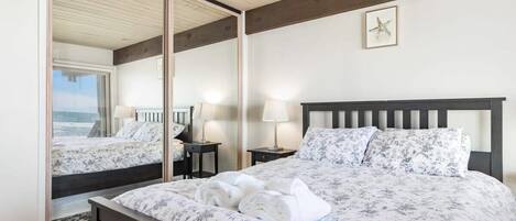 A bedroom with a large bed, a nightstand, a mirror, and a view of the ocean.