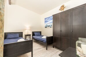 A bedroom with two single beds, a wardrobe, a nightstand, a lamp, and a wall art piece. - Sand Dollar Beachfront Home, Direct Beach Access! (La Selva Beach)