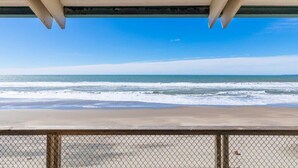 Une vue sur la plage depuis un espace abrité, délimité par une clôture en treillis métallique.