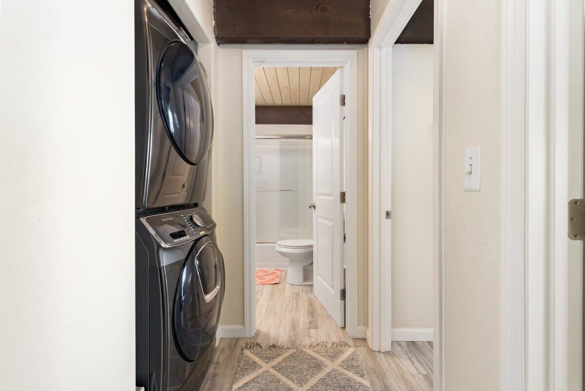 A laundry room with stacked washers and dryers, a shower room with a white toilet, and a rug on the floor.