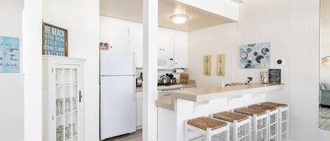 Une cuisine moderne avec des meubles blancs, un îlot central doté de tabourets de bar et un four à micro-ondes placé au-dessus de la cuisinière.
