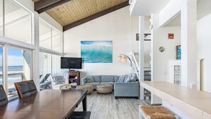 A spacious living area with a large window overlooking the ocean, a comfortable seating arrangement, and a flat-screen TV mounted on the wall. - Sand Dollar Beachfront Home, Direct Beach Access! (La Selva Beach)