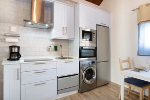 A compact kitchen with white cabinets, a stainless steel oven, a built-in washing machine, and a small dining area with a table and chair.