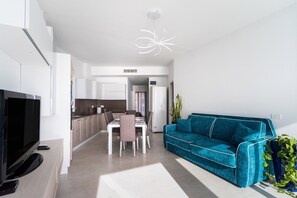 Un salon moderne avec un téléviseur, un canapé, un coin repas et une cuisine en arrière-plan.