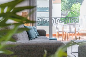 Un balcon avec un canapé et des fauteuils, une lampe en osier et une vue sur les immeubles et les arbres.