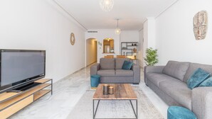 A modern living room with a flat-screen TV, two sofas, a coffee table, and a dining area in the background. - Apartment "Avenida Masnou" close to the Sea with Shared Pool & Wi-Fi (Calpe)