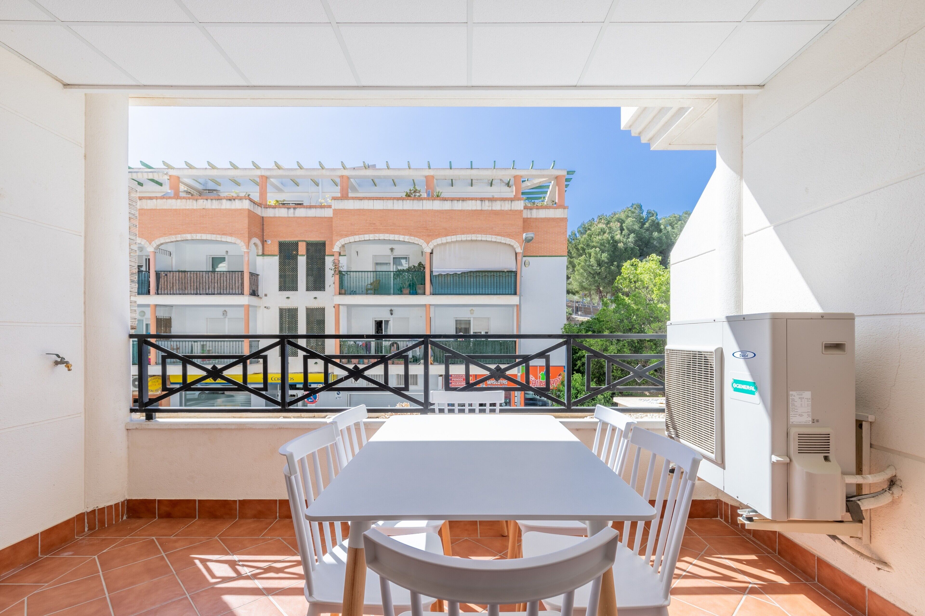A balcony with a white table and chairs, a view of a building with balconies, and an air conditioning unit.