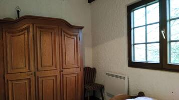 Ein Schlafzimmer mit großem Holzschrank, einem Sessel, einem Fenster mit Blick auf Bäume und einer Heizung.