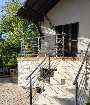 A staircase leading to a covered outdoor area with a metal railing, a white plastic chair, and a gas pump.