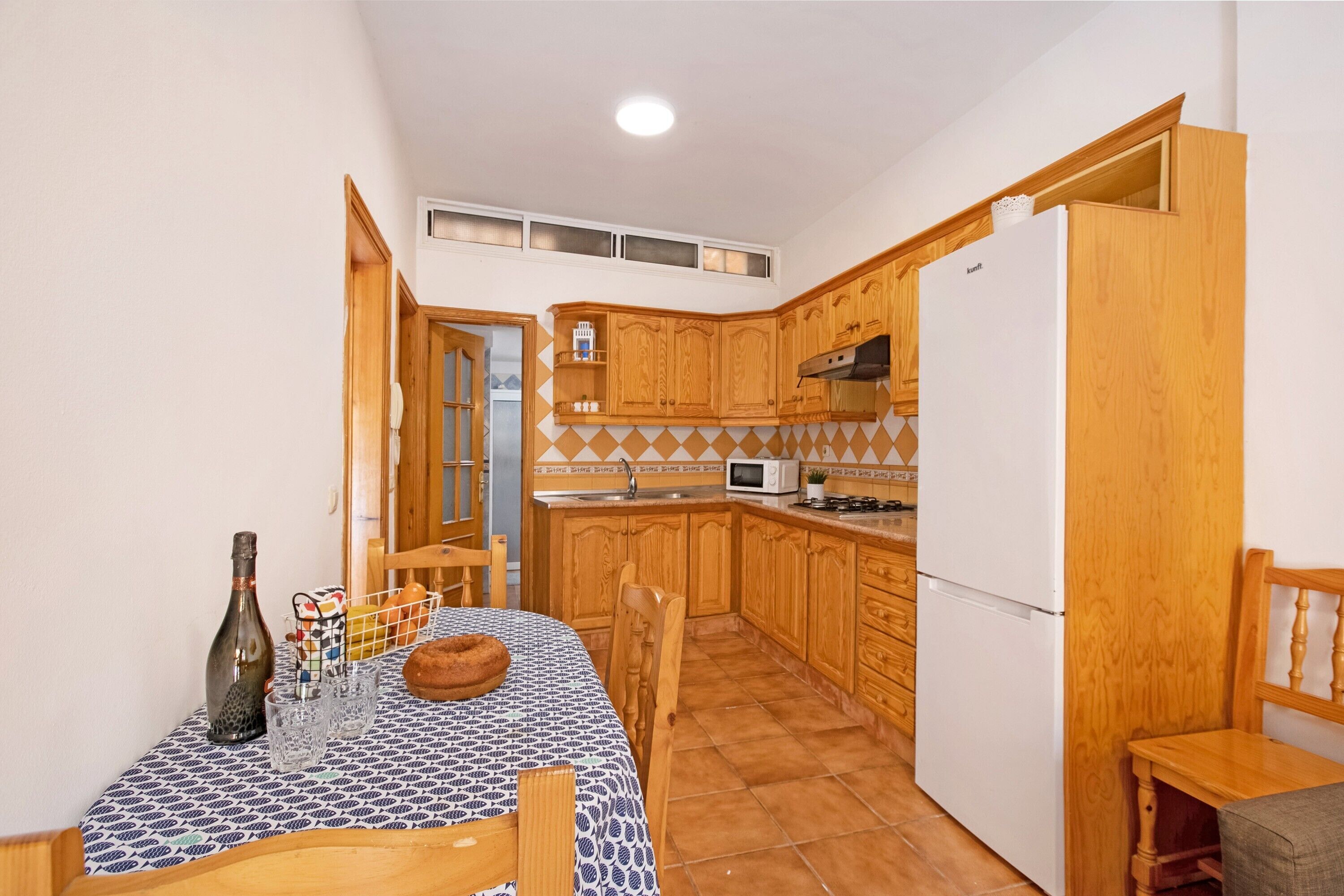 Una cocina compacta con armarios de madera, un refrigerador, un microondas y una mesa de comedor con sillas.