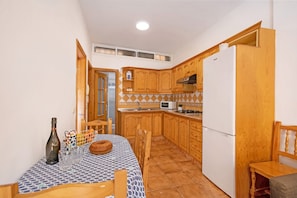 Uma cozinha compacta com armários de madeira, geladeira, micro-ondas e uma mesa de jantar com cadeiras.