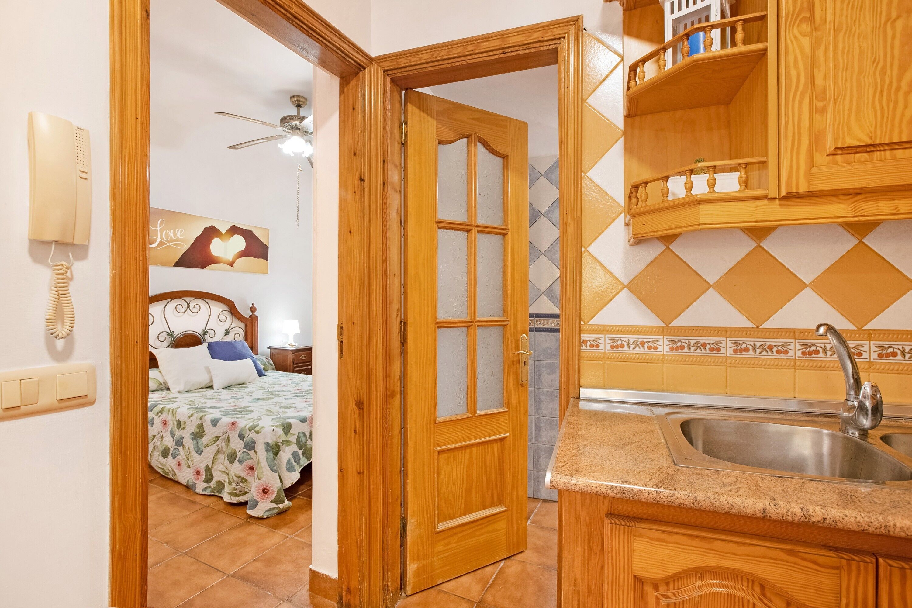 Ein Zimmer mit einem Bett, einer Holztür, einer Küchenzeile mit Spüle und einem an der Wand befestigten Telefon.