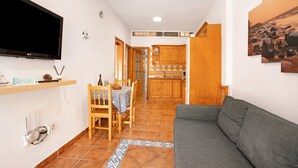 A living room with a grey sofa, a TV mounted on the wall, a dining area with a table and chairs, and a kitchen with wooden cabinets. - Vacation Home "Las Arenas Bajo" close to the Sea with Wi-Fi (Las Arenas)